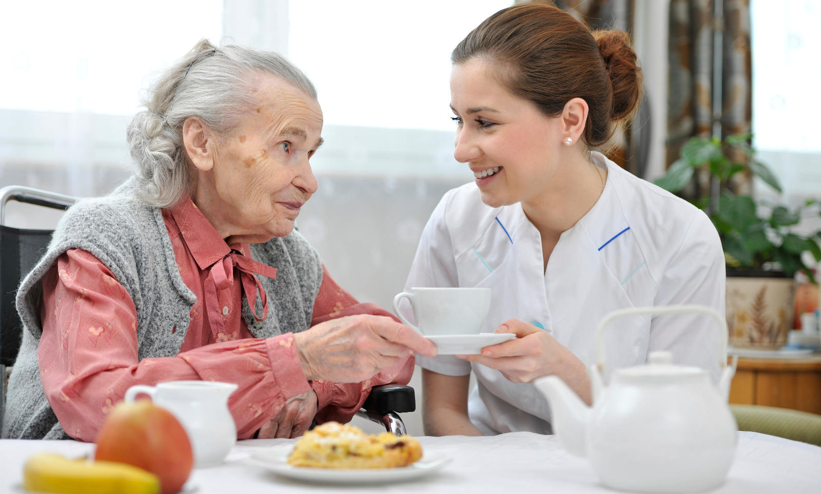 elderly woman having tea with female caregiver